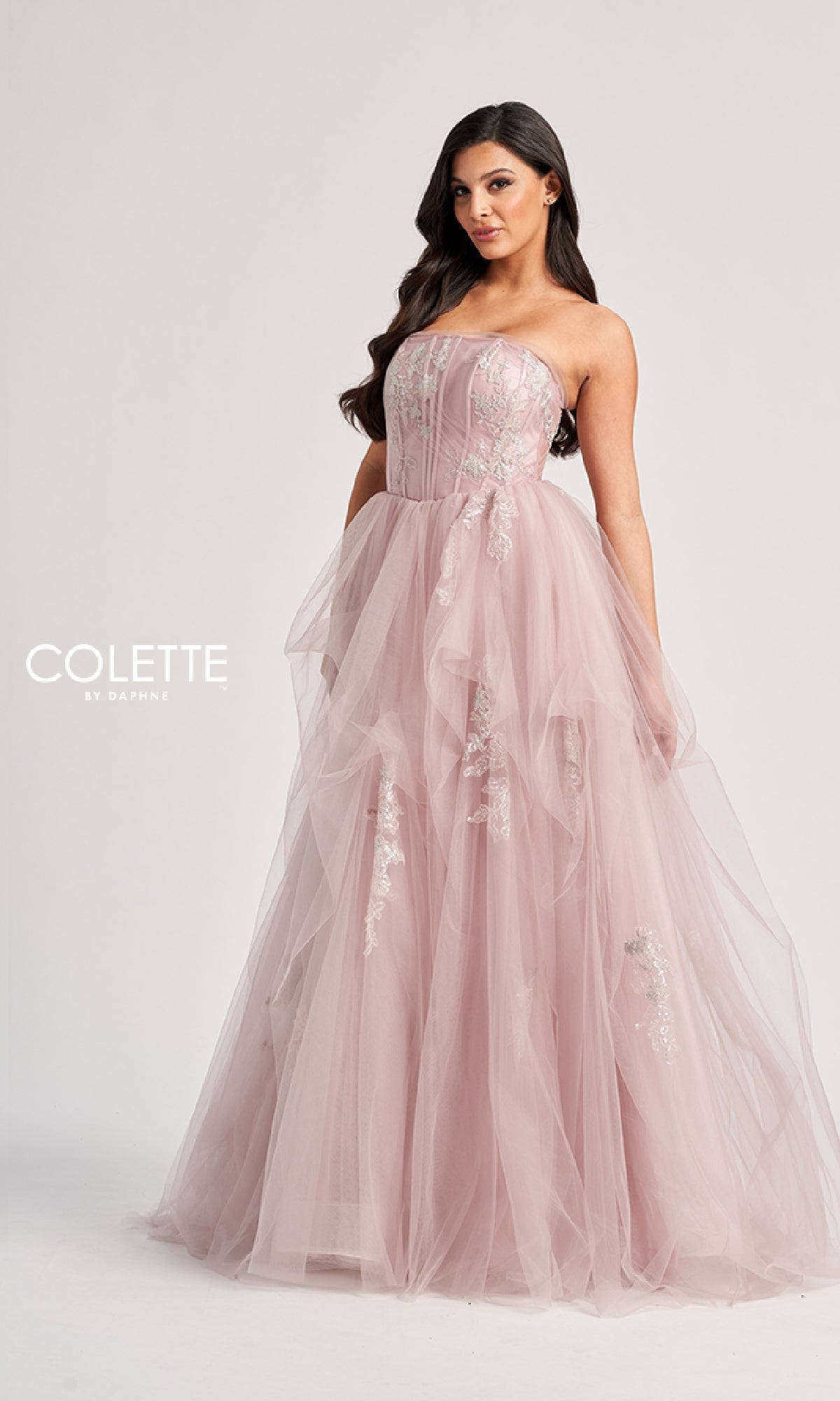 Woman wearing the Colette CL8120 long prom dress, featuring a strapless bodice, tulle A-line skirt, and delicate floral embellishments. Standing against a plain backdrop with